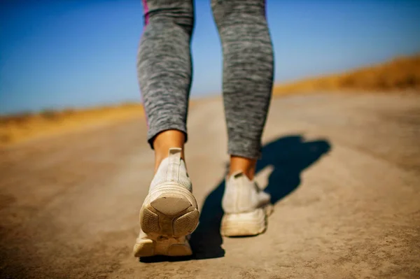 Runner feet running on road closeup on shoe. Woman fitness sunet jog workout welness concept .