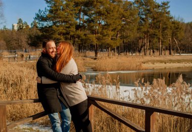 Couple in a winter forest and frozen lake. Young lovers in winter jackets laugh.