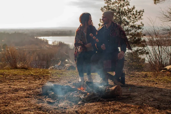 Romantic couple sitting at the campsite. Man and woman sitting on a log at campsite with bonfire in front.