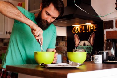 Sakallı bir gencin portresi. Evdeki mutfakta baş parmak işareti yapıyor..