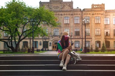 Üniversitenin yakınında maske takan öğrenci akıllı telefondan bakıyor..