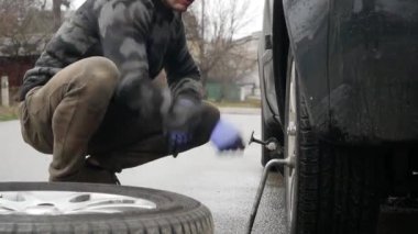 Genç adam yoldaki arabanın tekerleğini değiştiriyor..