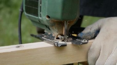 Bir adam elektrikli testereyle avluda kereste kesiyor..