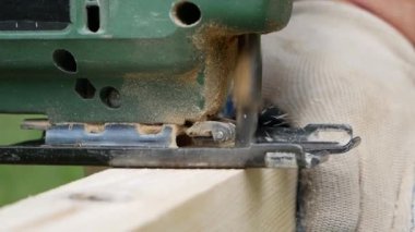Bir adam elektrikli testereyle avluda kereste kesiyor..