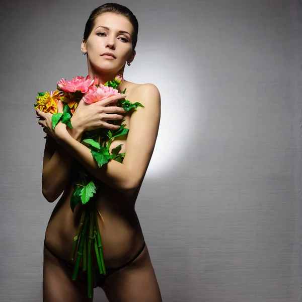 Νέοι σέξι αισθησιακή γυναίκα ή κορίτσι με μελαχρινή μαλλιά και όμορφο πρόσωπο τόπλες εκμετάλλευση λουλούδια στο γυμνό σώμα με εσώρουχα σε φόντο γκρι — Φωτογραφία Αρχείου