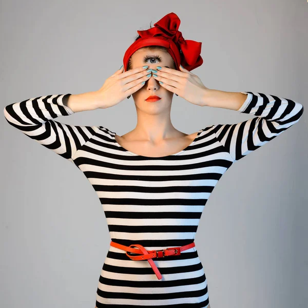 Mooi meisje in een gestreepte jurk en een rode tulband op haar hoofd bedekt zijn ogen met handen en esoterische Kottonmouth kijkt op haar voorhoofd — Stockfoto