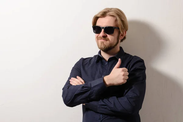 Stylischer Mann mit schwarzer Sonnenbrille, der mit verschränkten Armen an einer weißen Wand steht — Stockfoto