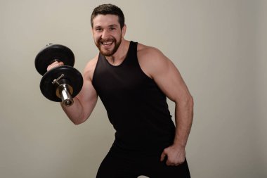 Genç gülümseyen atlet dumbbells ile bir egzersiz el kaslarının gelişimi üzerinde gerçekleştirir.