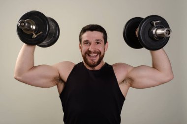 Acımasız gülümseyen adam vücut geliştirmeci atlet içinde dumbbells ile bir arka plan üzerinde eller