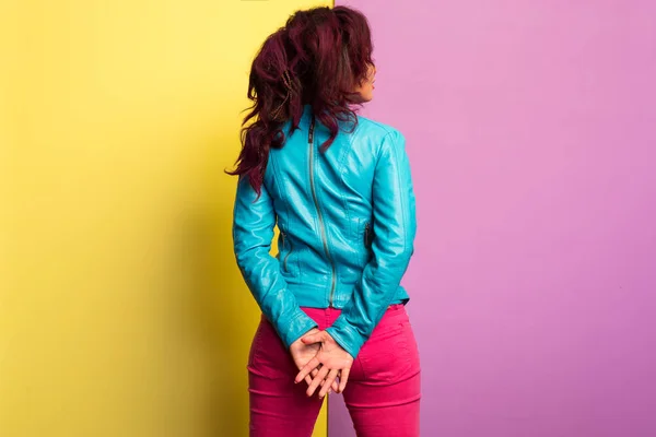 Hermosa mujer joven con el pelo morado con chaqueta de cuero azul y jeans magenta. pose de pie, aislado sobre fondo de color . — Foto de Stock