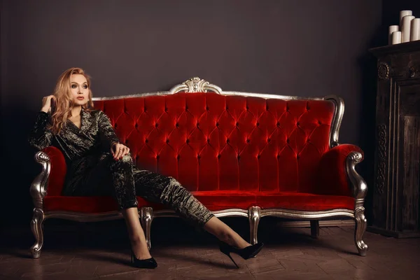 Belle jeune femme en costume velours assise sur un canapé vintage rouge — Photo