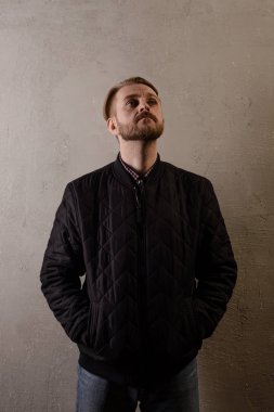 Bir çekici orta yaşlı sakallı bir siyah ceket ve kot duvar llooks savunur