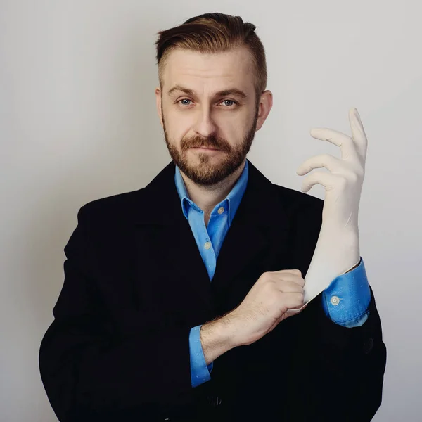 Attraktiver bärtiger Geschäftsmann in Anzug und blauem Hemd zieht Medizinhandschuh an — Stockfoto
