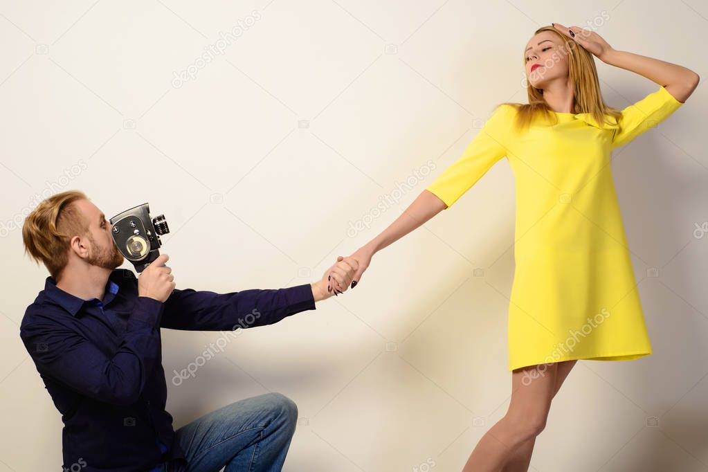 Stylish man in a blue shirt is filming a slim woman in a yellow dress