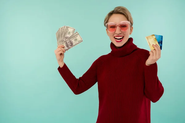 Portrait of happy young woman holding credit card and money in hand smiling and looking at camera