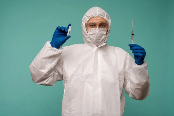 A male doctor in protective overalls and a mask holds an ampoule with a vaccine in his hands. Coronovirus protection concept in China.