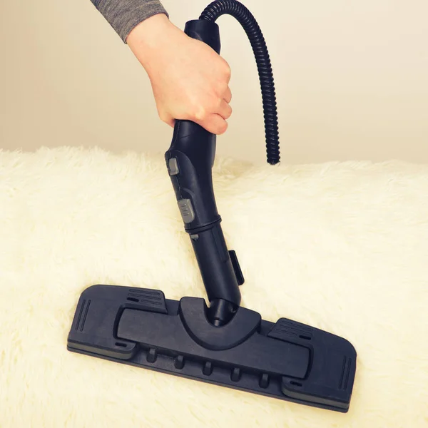 Young woman with a steam cleaner cleans the carpet on the couch