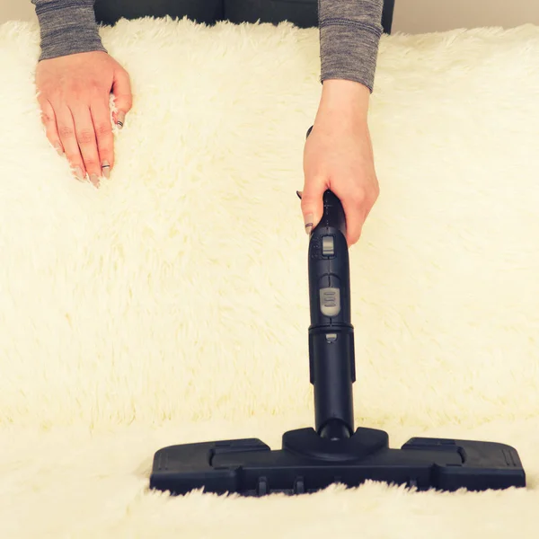 Young woman with a steam cleaner cleans the carpet on the couch