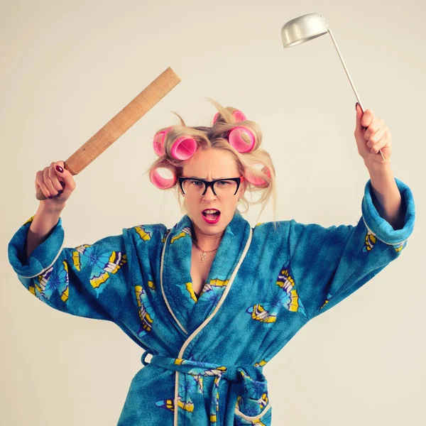 Screaming angry housewife in a dressing gown and curlers with a ladle in her hand.