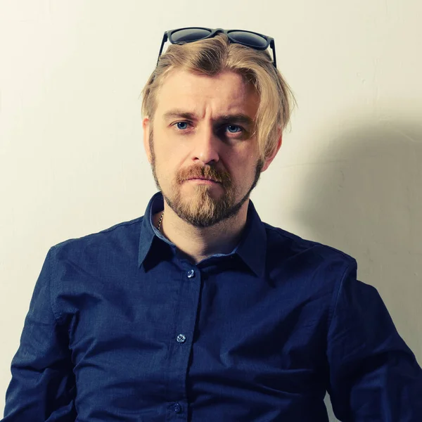 Attractive man in blue shirt and sunglasses on her head standing near a white wall