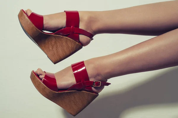 Beautiful female legs in red sandals on a wedge on white background