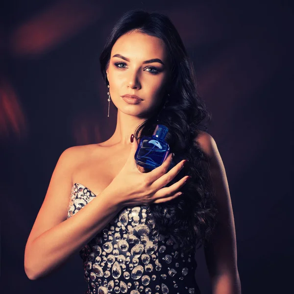 Beautiful young woman in a shiny dress holding a bottle of perfume.