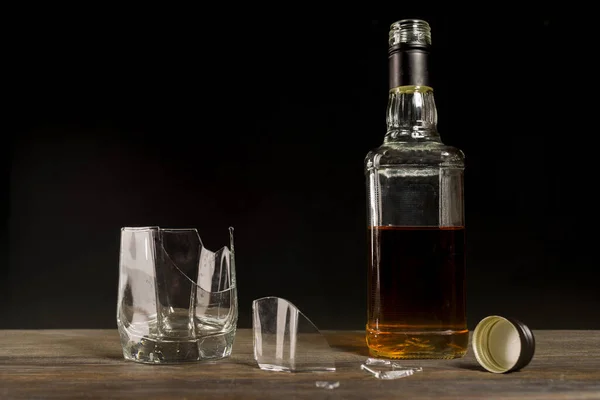 Broken glass and a bottle of whiskey. The concept of ruined life due to alcoholism. - image