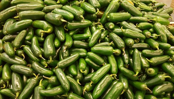 Green Jalapeno chili peppers loosely stacked into a market stand ready for sale. Raw spicy food ingredients.