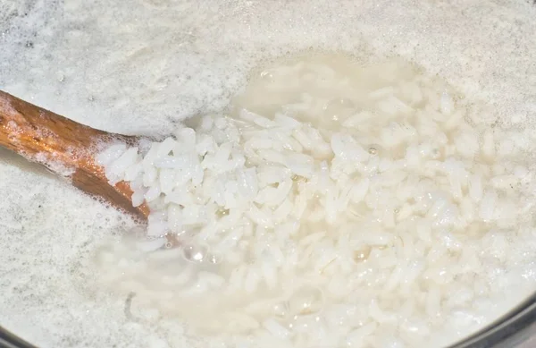 白いご飯の鍋に鍋に水を沸騰木製のスプーンでいくつかの米をすくう — ストック写真