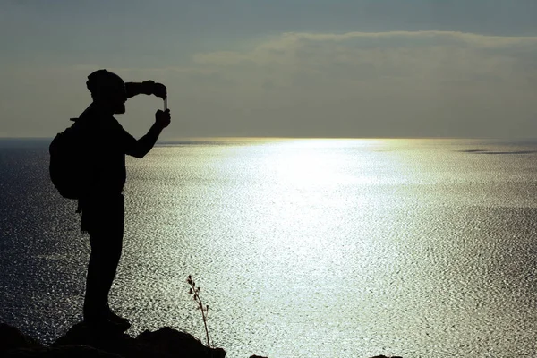 Silhouet van de mens staande op een rots en kijken op zee — Stockfoto