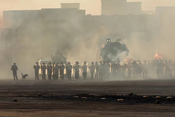 A polícia militar se alinha em resposta a um protesto com gás lacrimogêneo, fumaça, fogo, explosões e cães policiais. Expressão política, motim, protesto, manifestação e conceito militar . — Fotografia de Stock