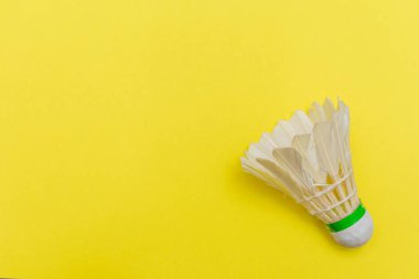 Badminton mekik ya da kuşçuğu düz sarı düz bir zeminde uzanmış, kopya alanı ile spor ve aktiviteyi sembolize ediyor..