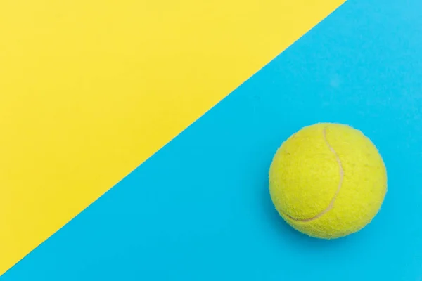 Желтый теннисный мяч на сплошной ярко-голубой и желтый плоский фон символизирует спорт и деятельность с копировальным пространством . — стоковое фото