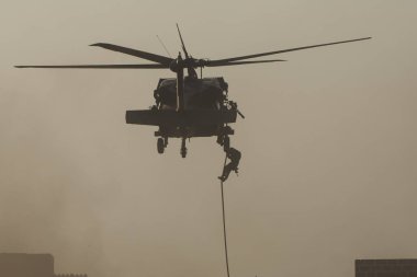 Kargaşa ve yıkımın içine uçan helikopterle askeri çatışma ve savaş. Askerler ipten yere kadar helikopterden askıya alınır. Askeri güç kavramı, güç, güç, hava saldırısı.