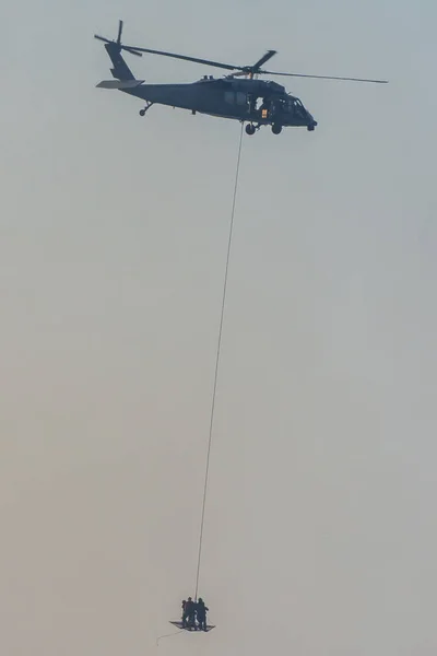 Militärteam im Konflikt, das Menschen per Hubschrauber rettet. durch die Luft fliegen an einem Seil, das am Hubschrauber befestigt ist, im Rauch und Dunst des Nahost-Konflikts. — Stockfoto