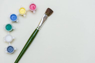 Yeşil ve beyaz boya fırçaları ve canlı renkli su renkleriyle bembeyaz sanat yassı kavramı yaratıcılığı, ilhamı ve sanatsal ifadeyi resmeder..