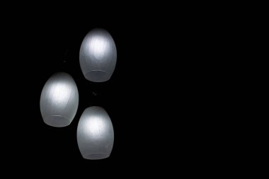 Üç parlak ışıklı konut ampulü siyah arka planda karanlık bir odayı aydınlatıyor. İş, hedef belirleme, enerji tasarrufu kavramları.