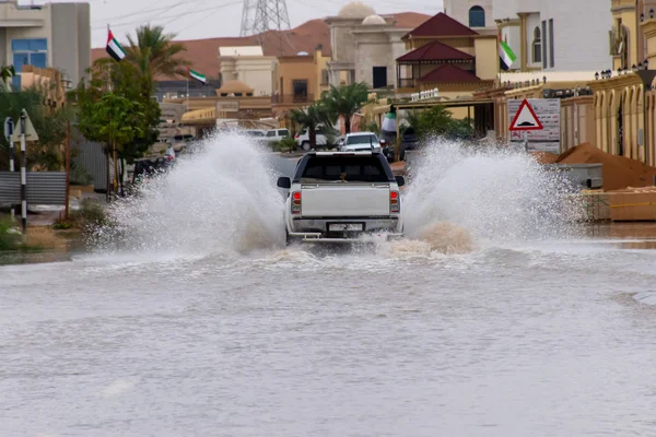 Kuorma-auto ajaa tulvavesien läpi kadulla tehden suuria vesipisaroita asuinalueella . — kuvapankkivalokuva