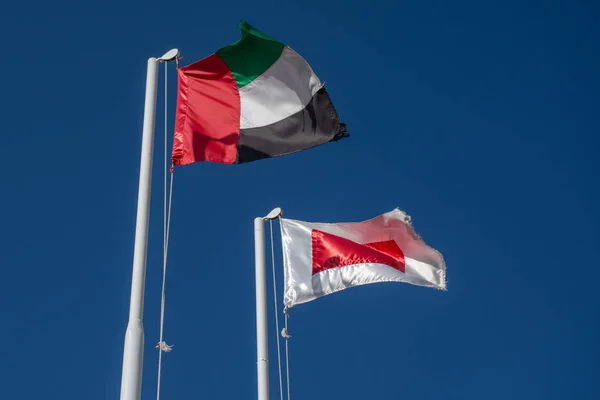 Ras al Khaimah flag (red and white) in the United Arab Emirates (UAE) north of Dubai, and  UAE flag blowing in the wind on a blue sky background. — Stock Photo, Image