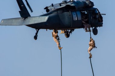 Kargaşa ve yıkımın içine uçan helikopterle askeri çatışma ve savaş. Askerler ipten yere kadar helikopterden askıya alınır. Askeri güç kavramı, güç, güç, hava saldırısı. UAQ Birlik Kalesi 7
