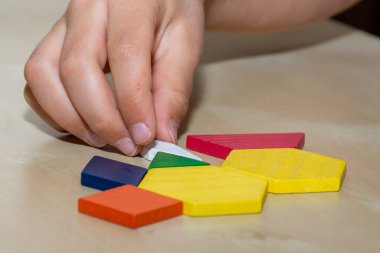 Tangram geometrik renkli şekiller, kahverengi arkaplan parçalarını elle dolduran yapboz parçaları.