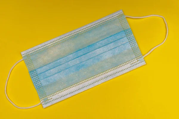 Blue medical face mask flat lay on bright yellow background for health care prevention and COVID-19 (Coronavirus) precaution.