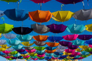 Mavi gökyüzü güneşli bir günde yürüyüş sokağında sallanan renkli canlı şemsiyeler.