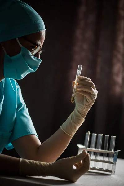 Conceptual photograph of a doctor holding and looking at a test tube while testing samples for presence of coronavirus (COVID-19).