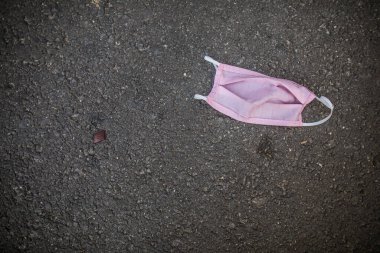 Kullanılmış pembe bir yüz koruma maskesi kaldırımda duruyor..