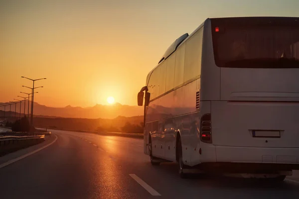 Ônibus branco dirigindo na estrada em direção ao pôr do sol — Fotografia de Stock
