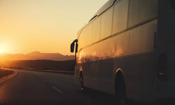 White bus driving on road towards the setting sun