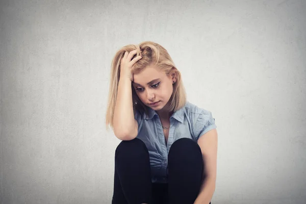 Een triest vrouw zittend op de vloer in de buurt van een muur en houden haar hoofd in haar handen — Stockfoto