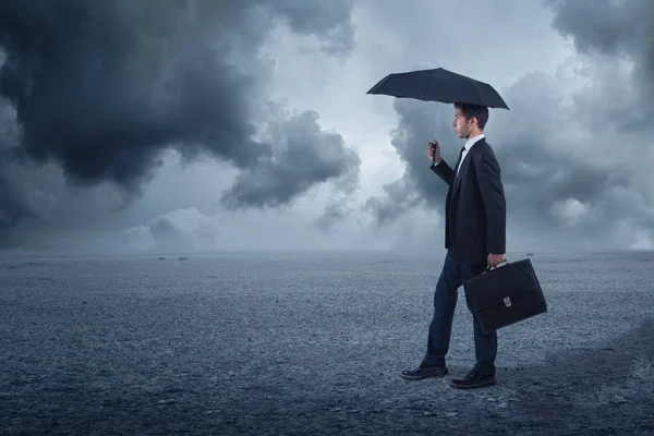 Zakenman met paraplu staande bij bewolkte achtergrond — Stockfoto