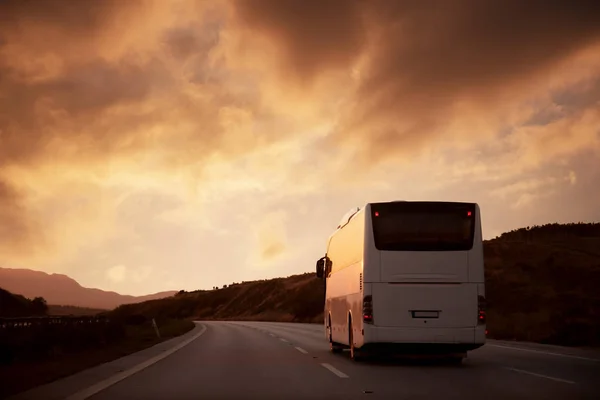 Белый автобус едет по дороге к заходящему солнцу — стоковое фото